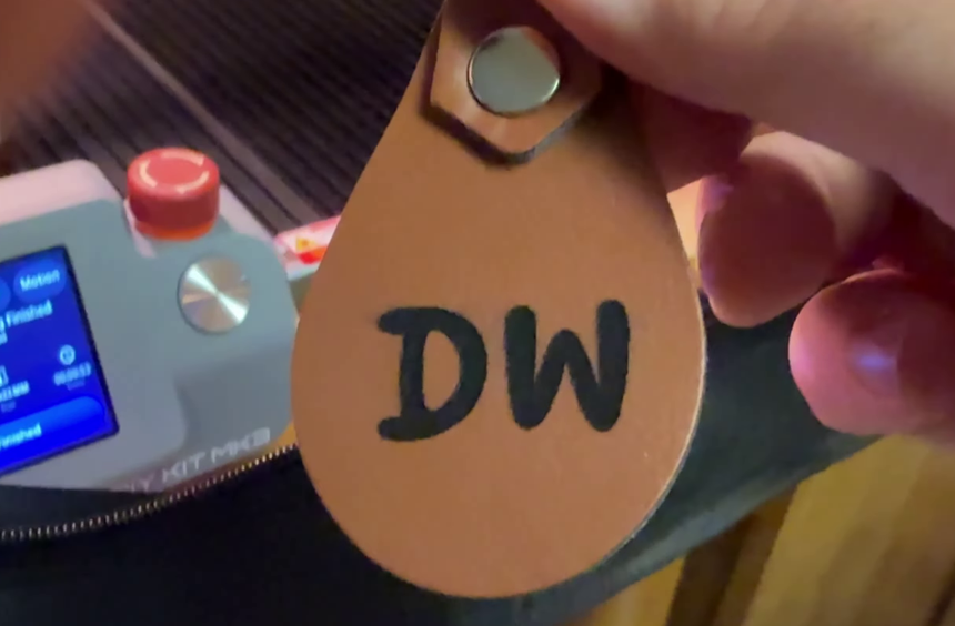 A leather keychain engraved with large initials, held in front of the machine's touchscreen