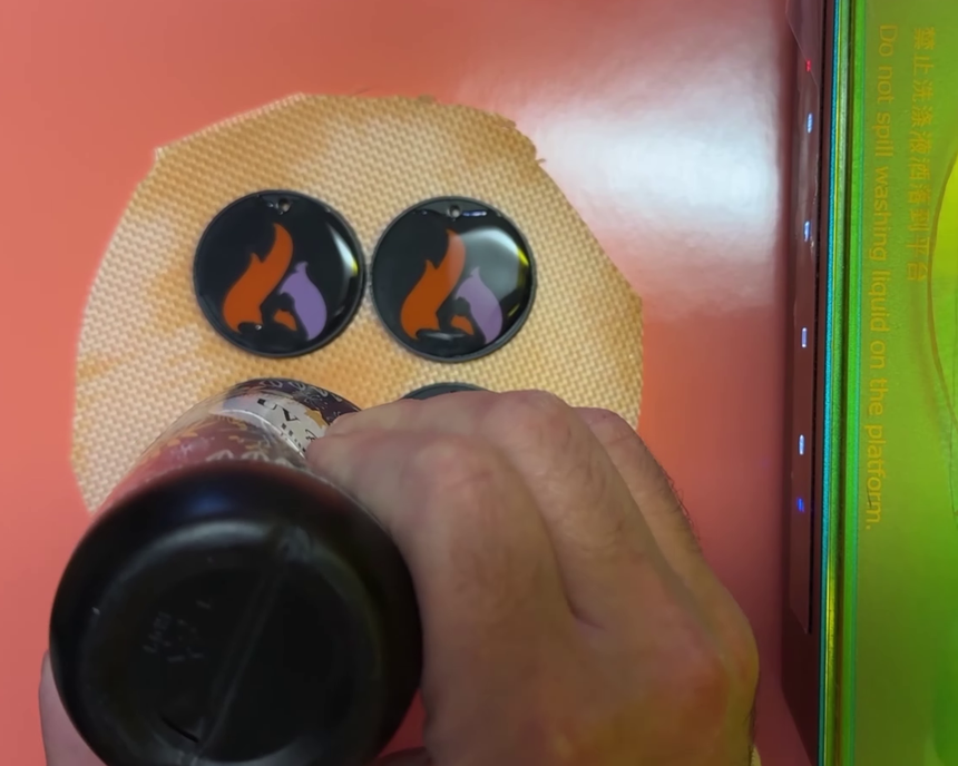 Resin being squeezed from a bottle into keychains sitting on a silicone mat beside a curing station