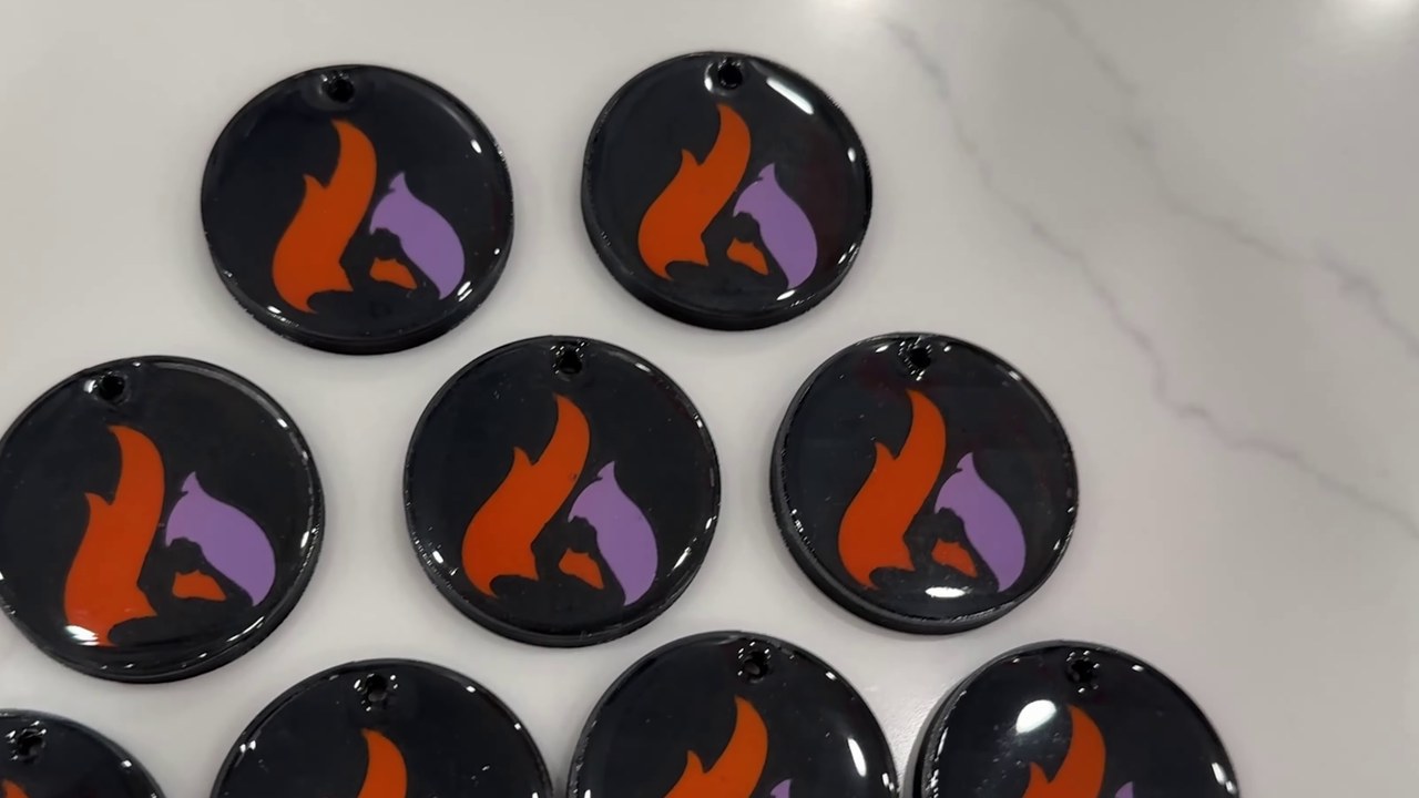 Nine finished black keychains with an orange and purple logo under a domed layer of clear resin